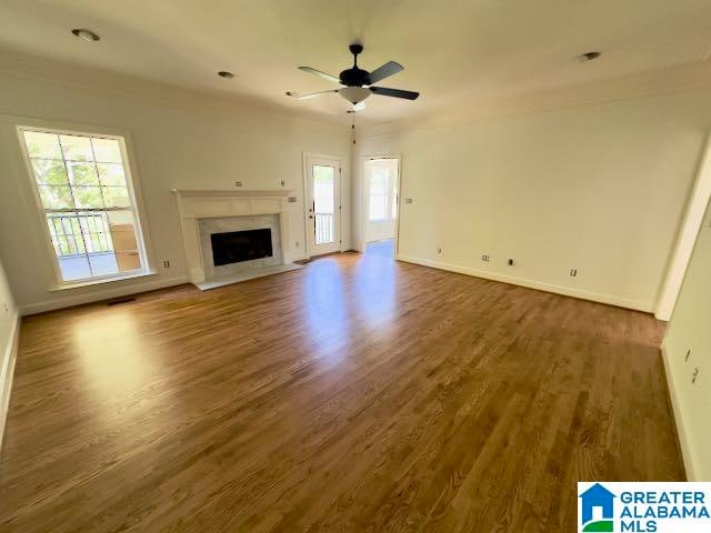 unfurnished living room featuring ceiling fan, dark wood-type flooring, a high end fireplace, and a wealth of natural light