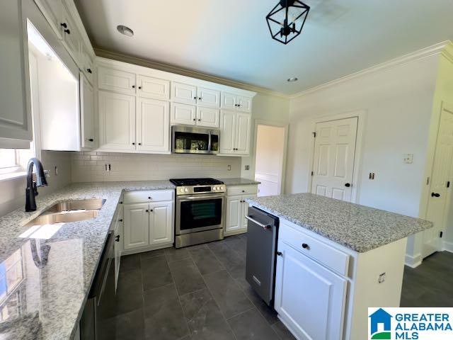 kitchen with light stone countertops, a center island, sink, white cabinetry, and appliances with stainless steel finishes