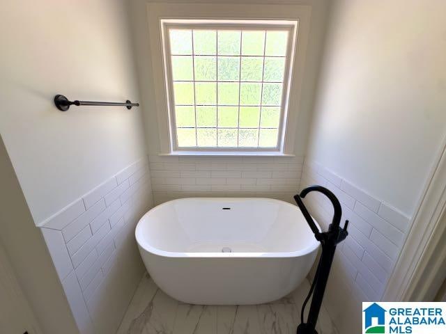 bathroom featuring a bathing tub, a wealth of natural light, and tile walls