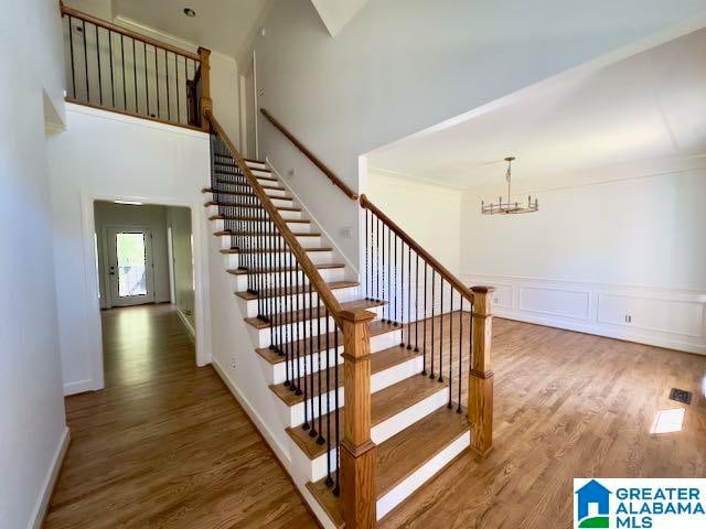 staircase featuring a towering ceiling, hardwood / wood-style floors, and an inviting chandelier