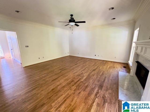 unfurnished living room with ceiling fan, a premium fireplace, dark hardwood / wood-style flooring, and crown molding