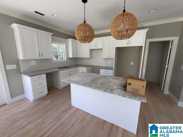 kitchen with white cabinetry, crown molding, a center island, pendant lighting, and light stone countertops