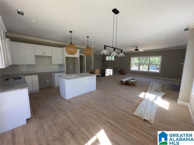 kitchen featuring white cabinetry, tasteful backsplash, decorative light fixtures, a center island, and light hardwood / wood-style flooring