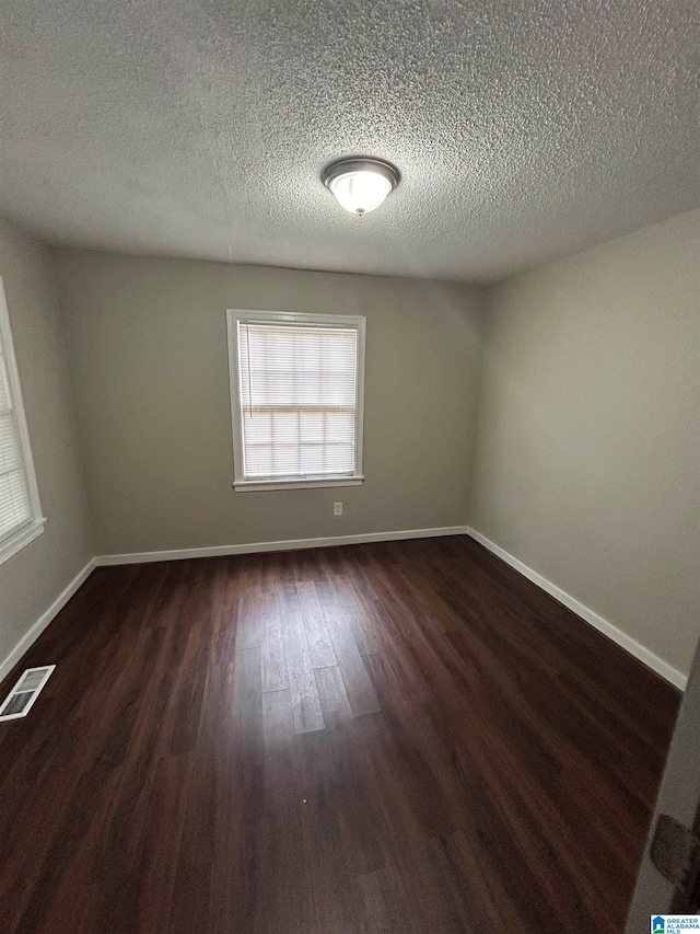 empty room with dark wood-type flooring and a textured ceiling