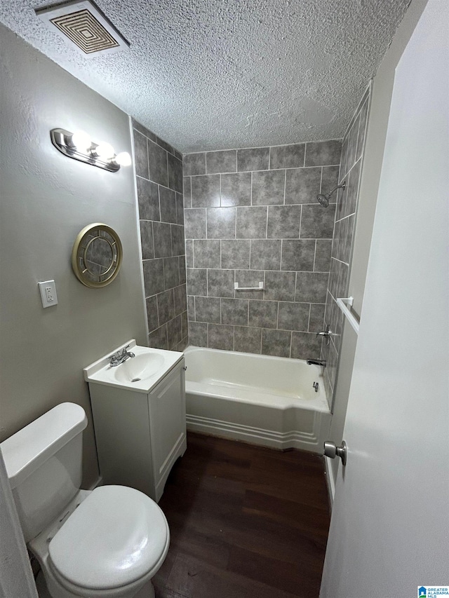 full bathroom featuring vanity, hardwood / wood-style flooring, tiled shower / bath combo, toilet, and a textured ceiling