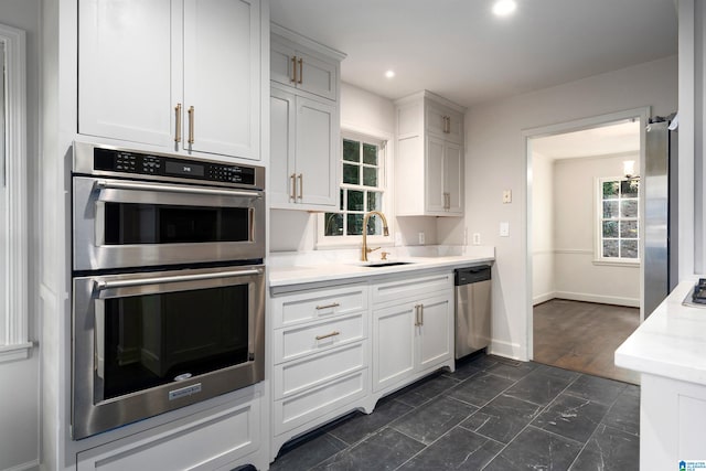 kitchen with a sink, white cabinets, light countertops, appliances with stainless steel finishes, and plenty of natural light