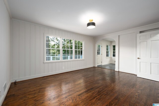 empty room featuring arched walkways, dark wood finished floors, visible vents, and crown molding