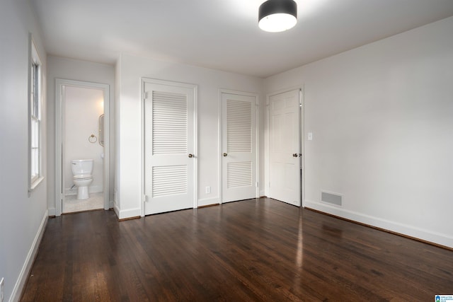 unfurnished bedroom with multiple closets, visible vents, dark wood-type flooring, connected bathroom, and baseboards