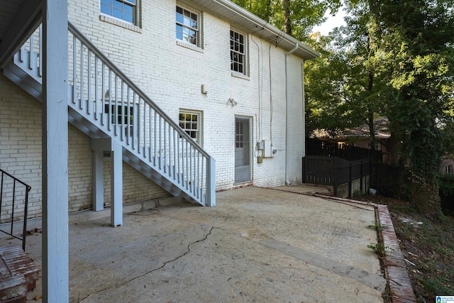 rear view of property with stairs, a patio, brick siding, and fence