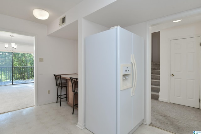 kitchen with a notable chandelier, light carpet, white fridge with ice dispenser, and hanging light fixtures