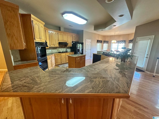 kitchen featuring light hardwood / wood-style floors, a center island, tasteful backsplash, and black appliances