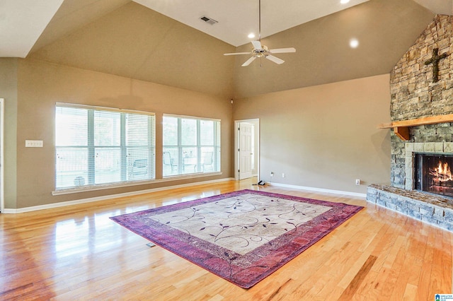 living room featuring high vaulted ceiling, a stone fireplace, wood-type flooring, and ceiling fan