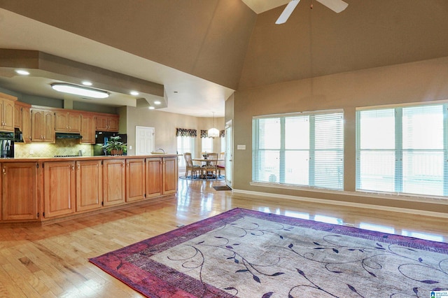 kitchen with decorative backsplash, black stovetop, light hardwood / wood-style flooring, high vaulted ceiling, and ceiling fan with notable chandelier