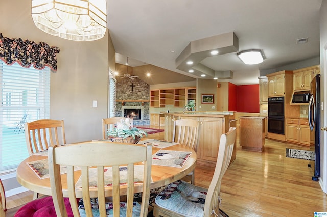 dining area featuring a notable chandelier, a stone fireplace, and light wood-type flooring