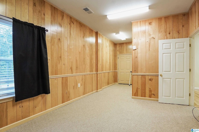 carpeted empty room with a healthy amount of sunlight and wood walls