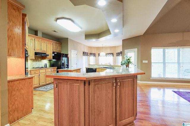 kitchen with decorative backsplash, hanging light fixtures, sink, black appliances, and light hardwood / wood-style floors