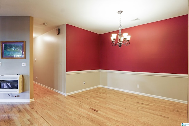 empty room with heating unit, a chandelier, and hardwood / wood-style floors