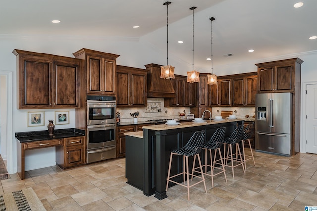 kitchen with stainless steel appliances, vaulted ceiling, pendant lighting, custom exhaust hood, and a center island with sink