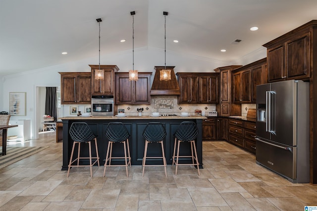 kitchen featuring a center island with sink, appliances with stainless steel finishes, vaulted ceiling, dark brown cabinetry, and decorative light fixtures