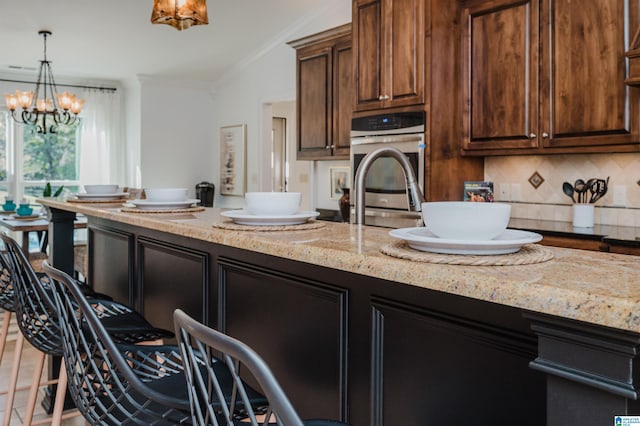 kitchen with crown molding, decorative light fixtures, an inviting chandelier, light stone counters, and tasteful backsplash