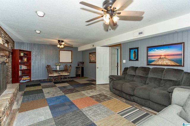 living room with a brick fireplace, a textured ceiling, and ceiling fan