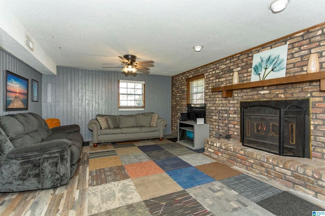 living room with ceiling fan, hardwood / wood-style flooring, a textured ceiling, and a brick fireplace