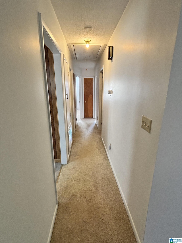 corridor with light carpet and a textured ceiling