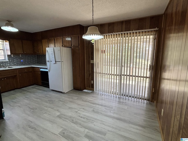 kitchen featuring decorative backsplash, light wood-type flooring, pendant lighting, white refrigerator, and wood walls