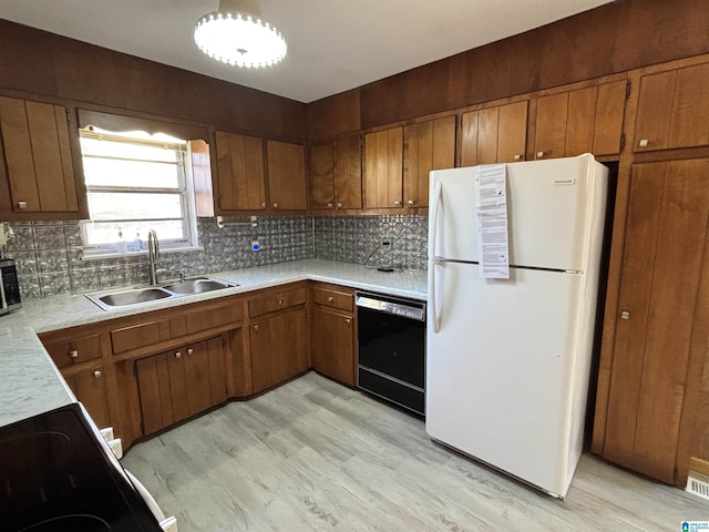 kitchen with sink, black dishwasher, light hardwood / wood-style flooring, white refrigerator, and backsplash