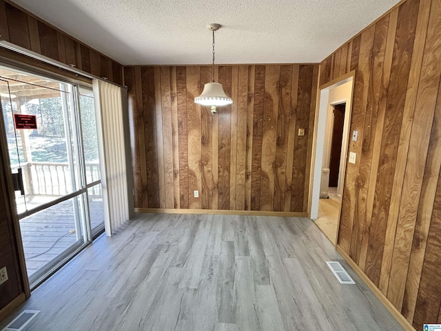 unfurnished dining area with wooden walls, light hardwood / wood-style floors, and a textured ceiling