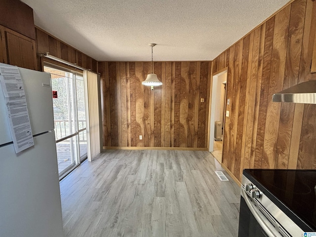 unfurnished dining area featuring wood walls, light hardwood / wood-style floors, and a textured ceiling