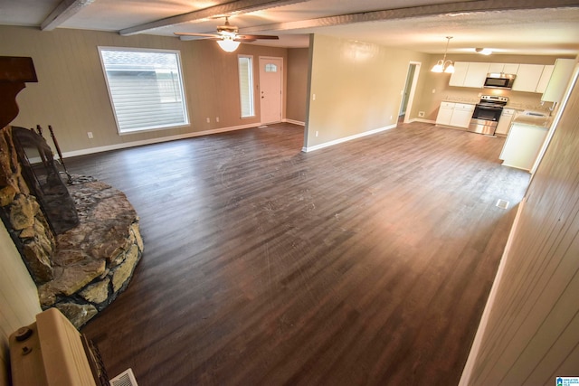 unfurnished living room with a stone fireplace, beamed ceiling, sink, ceiling fan with notable chandelier, and dark hardwood / wood-style flooring