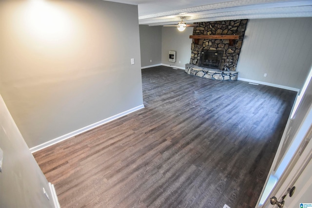 unfurnished living room featuring ceiling fan, a stone fireplace, heating unit, and dark hardwood / wood-style floors