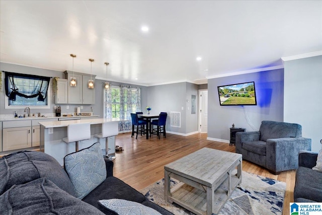 living room featuring crown molding, sink, and light wood-type flooring