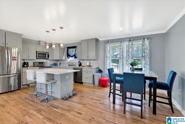 kitchen with appliances with stainless steel finishes, light hardwood / wood-style flooring, gray cabinets, decorative light fixtures, and a center island