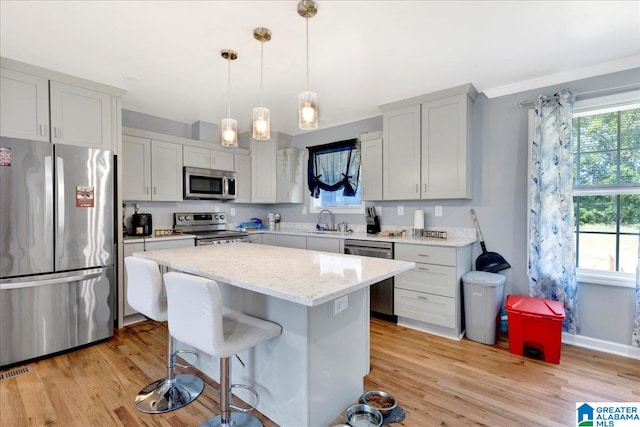 kitchen with hanging light fixtures, appliances with stainless steel finishes, sink, light hardwood / wood-style floors, and a center island