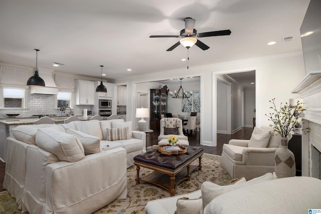 living room featuring ornamental molding, wood-type flooring, a fireplace, and ceiling fan with notable chandelier