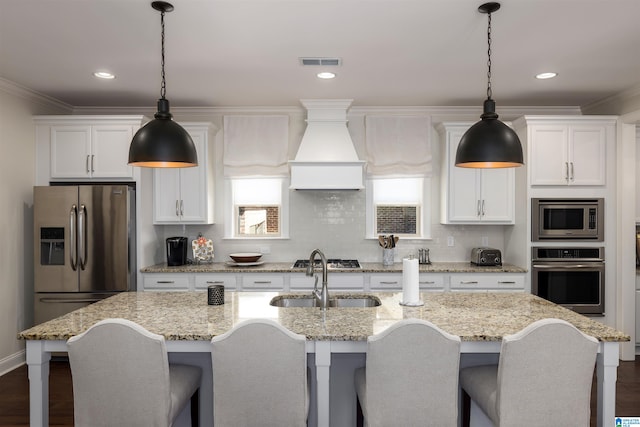 kitchen featuring a kitchen island with sink, pendant lighting, white cabinets, and stainless steel appliances