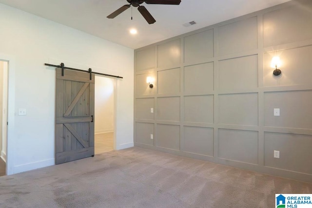 unfurnished bedroom with a barn door, light carpet, and ceiling fan