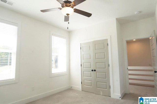 unfurnished bedroom with a closet, multiple windows, light colored carpet, and ceiling fan