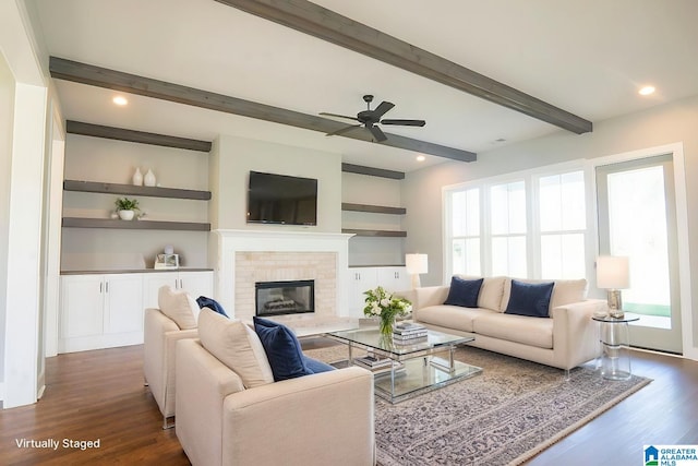 living room featuring ceiling fan, beamed ceiling, dark wood-type flooring, and a brick fireplace