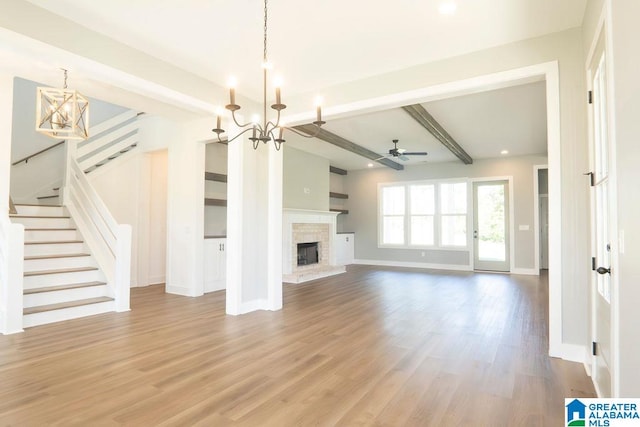 unfurnished living room featuring a wall mounted air conditioner, light hardwood / wood-style flooring, beam ceiling, and ceiling fan with notable chandelier