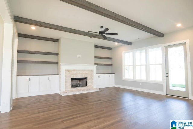 unfurnished living room featuring dark wood-type flooring, beam ceiling, a fireplace, and ceiling fan