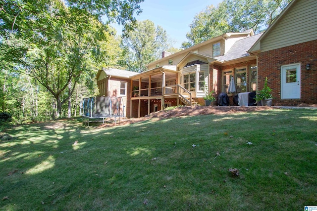 back of house with a lawn, a trampoline, and a sunroom