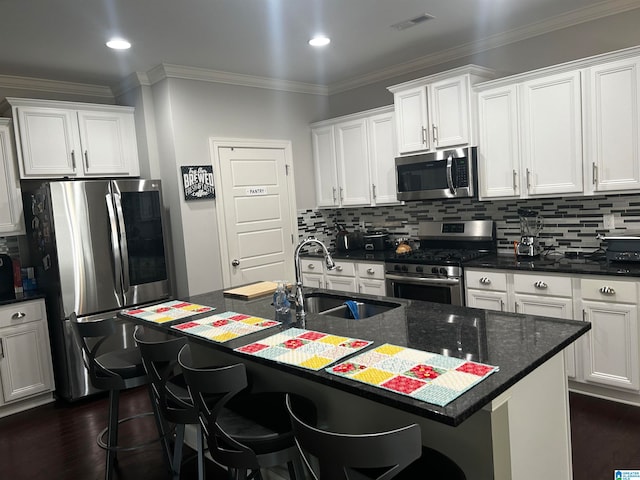 kitchen featuring white cabinetry, a kitchen island with sink, dark wood-type flooring, crown molding, and stainless steel appliances