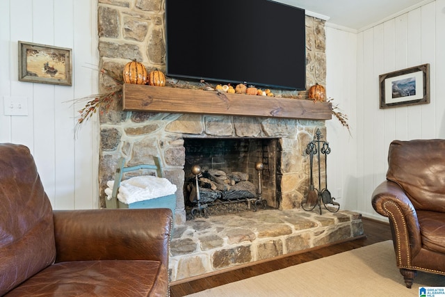 sitting room featuring a stone fireplace, wood walls, hardwood / wood-style flooring, and ornamental molding