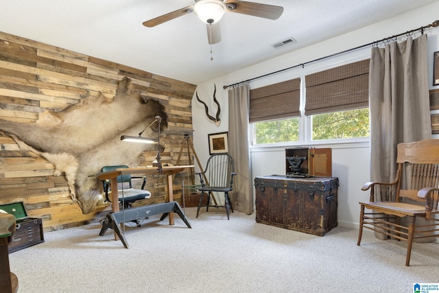 sitting room featuring light colored carpet, wood walls, and ceiling fan