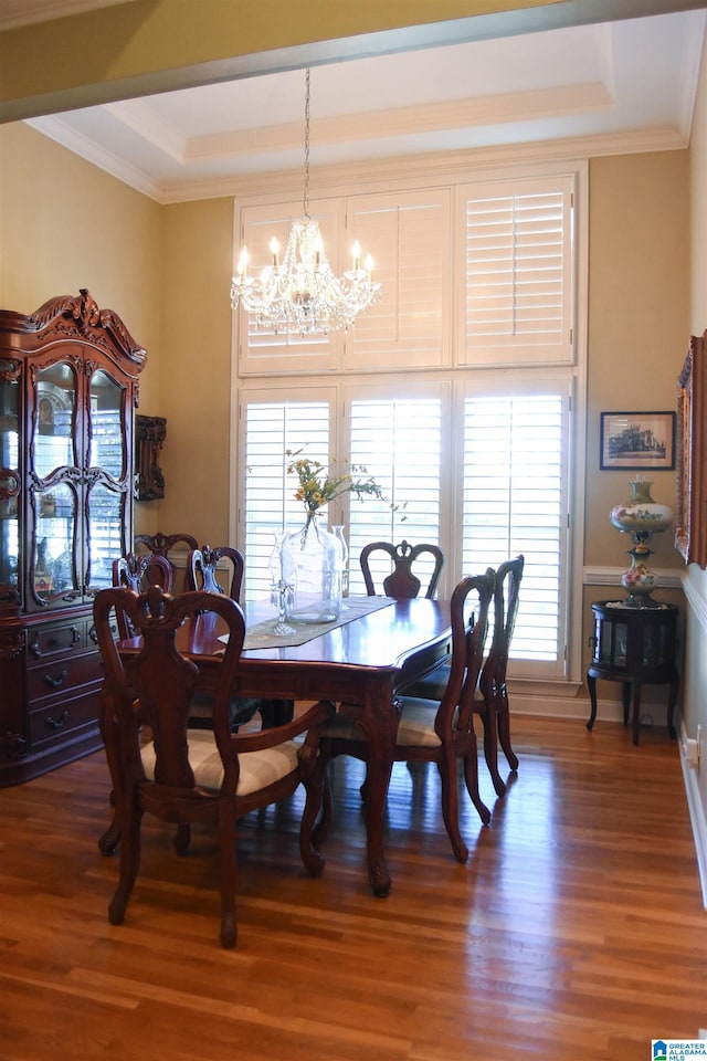 dining room with crown molding, hardwood / wood-style flooring, a tray ceiling, and an inviting chandelier