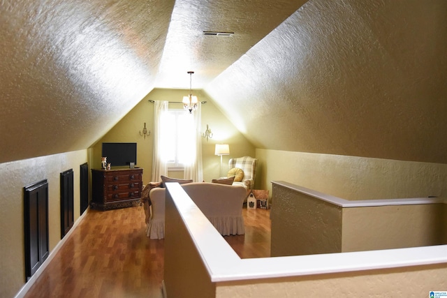 bonus room with hardwood / wood-style floors, a chandelier, a textured ceiling, and vaulted ceiling