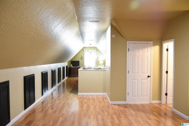 bonus room featuring light hardwood / wood-style floors, a textured ceiling, and lofted ceiling